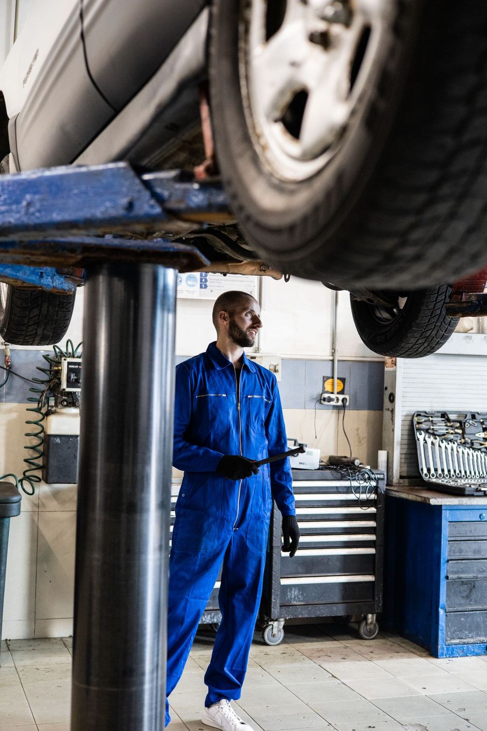 Technician standing under a car raised on a lift in a bright, modern auto service bay