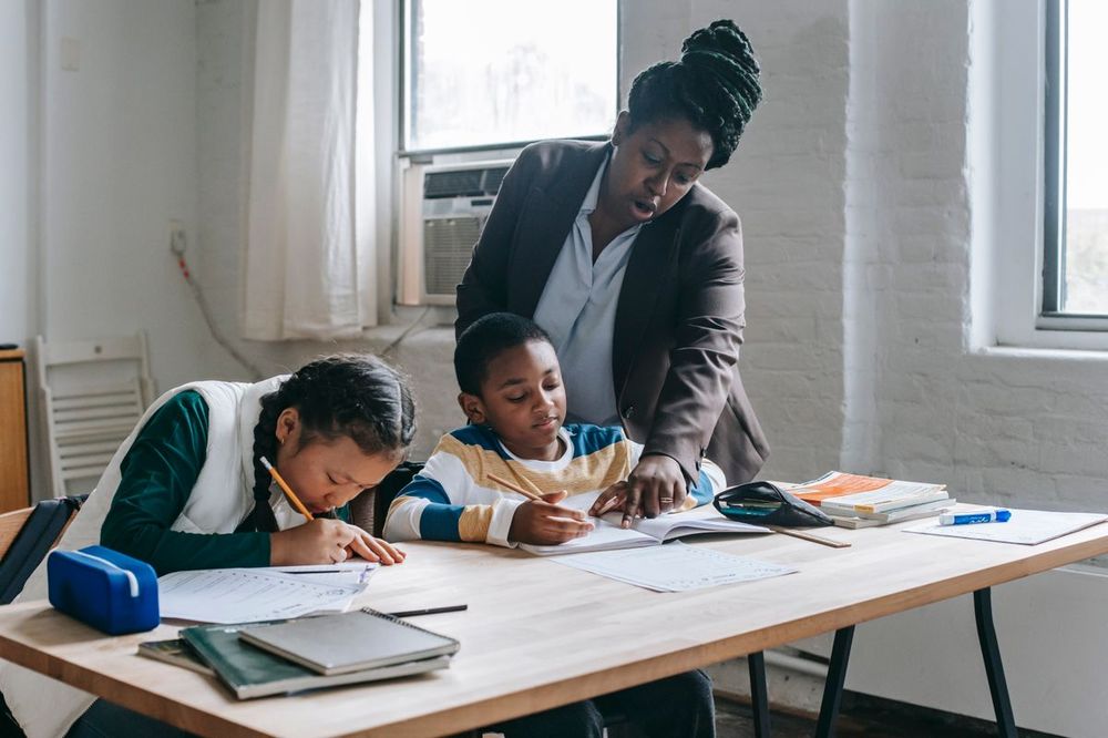 Teacher helping two students with their schoolwork at a classroom table