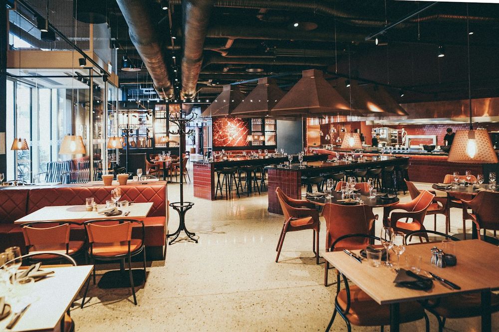 Warm, modern restaurant interior with set tables and an open kitchen